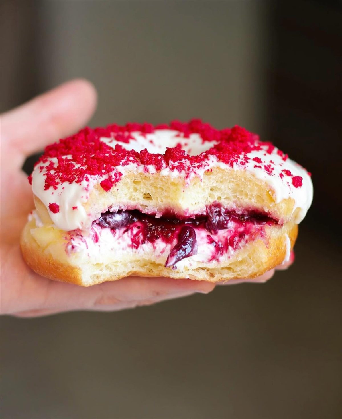 Donut recheado mordido, mostrando o recheio cremoso de frutas vermelhas por dentro