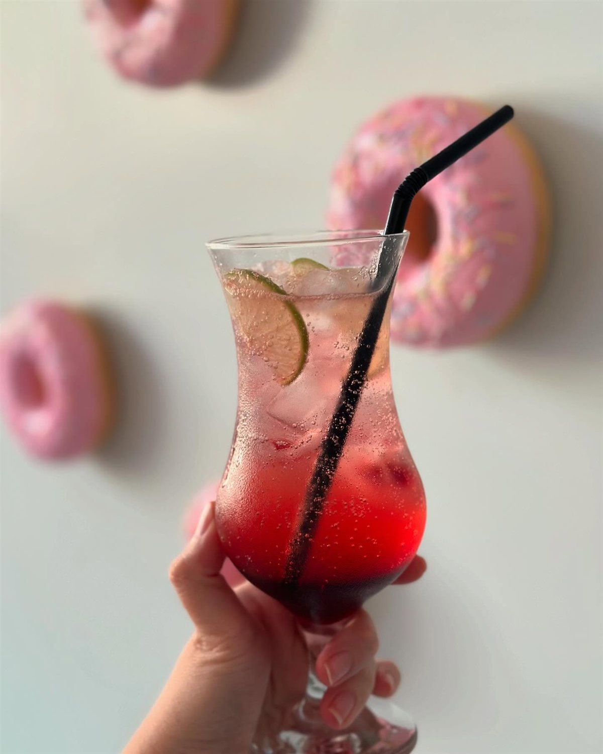 Drink gelado com limão e canudo, donuts rosa desfocados ao fundo
