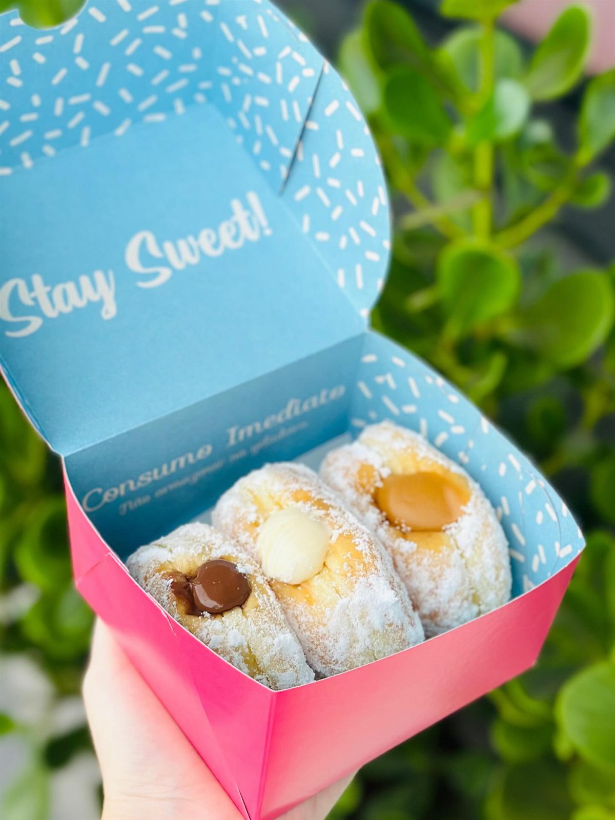 Caixa com três mini bombas cobertas de açúcar, recheadas de doce de leite, nutella e coco